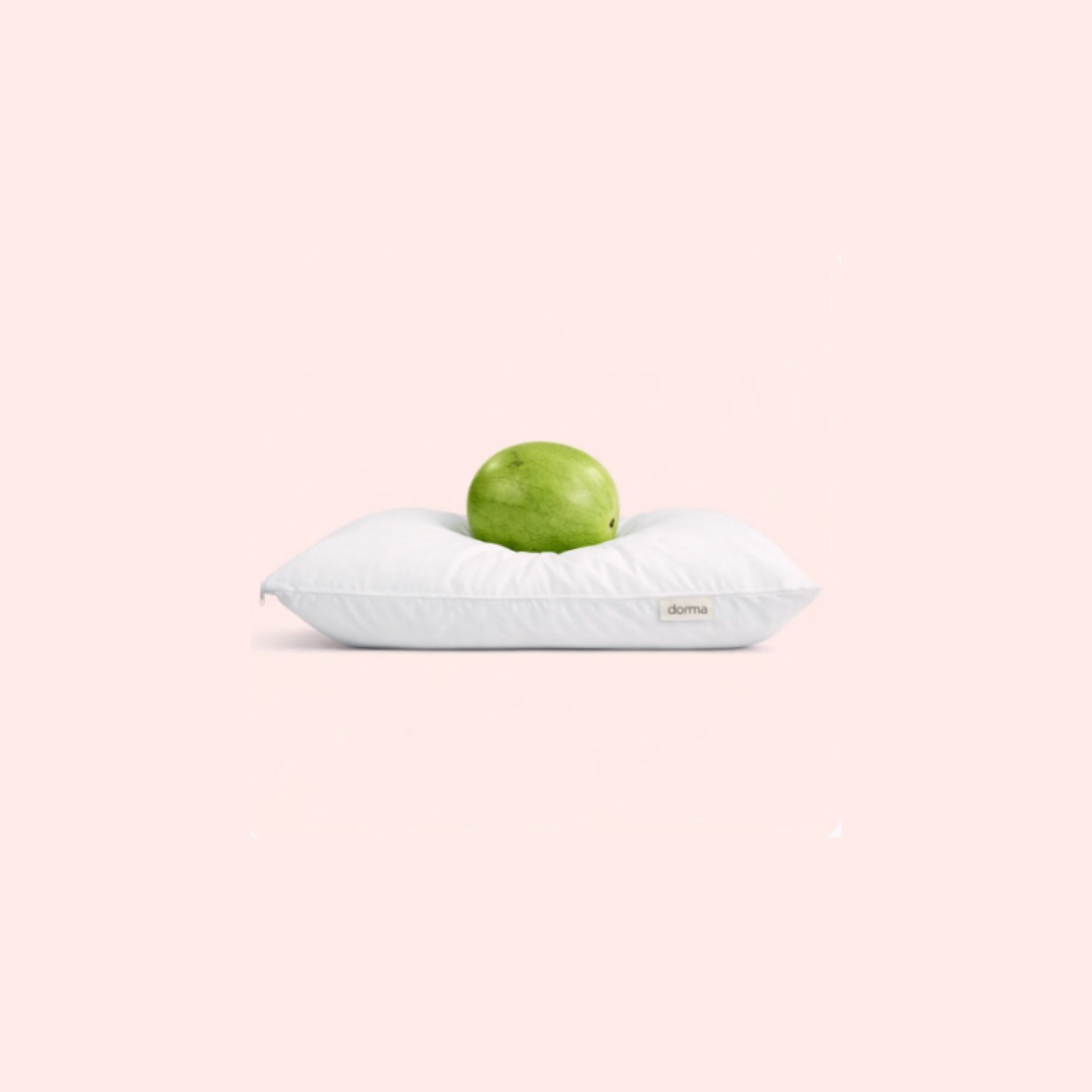Almohada blanca acolchada de Dorma con una manzana verde encima, sobre fondo rosa pálido