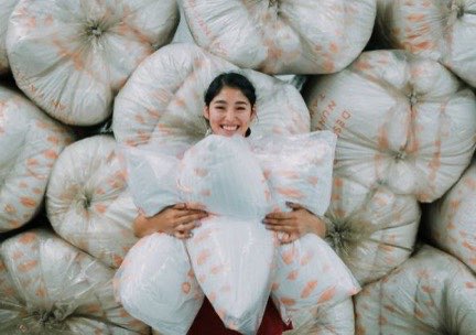 Una mujer sonriendo mientras abraza varias almohadas Dorma frente a una pila de fardos de producto