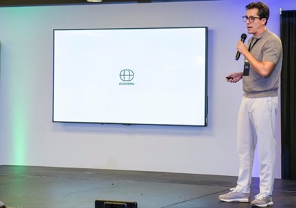 Edgar Temores con micrófono en un escenario, junto a una pantalla que muestra el logotipo de EcoHero
