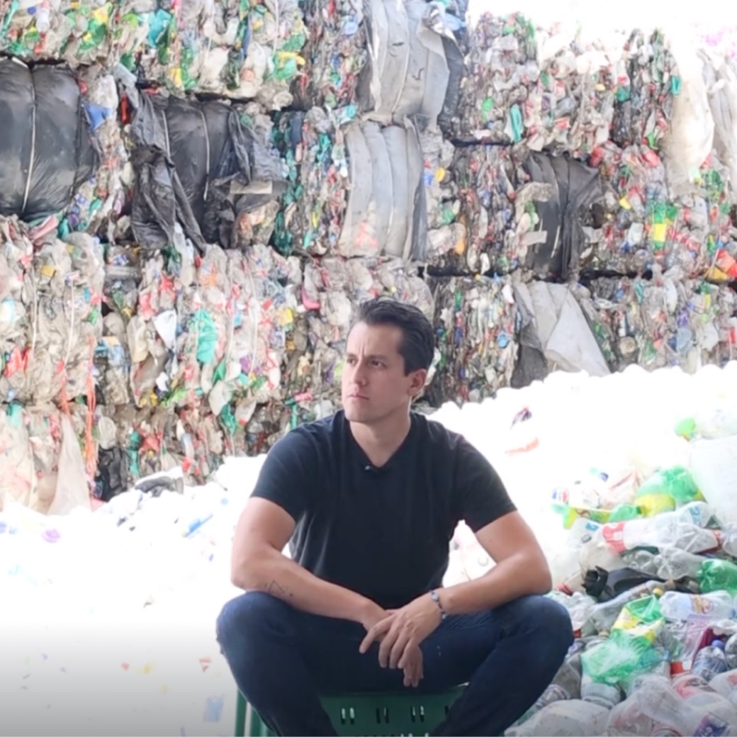 Edgar Temores sentado entre pacas de PET y botellas de plástico recolectadas en una planta de reciclaje