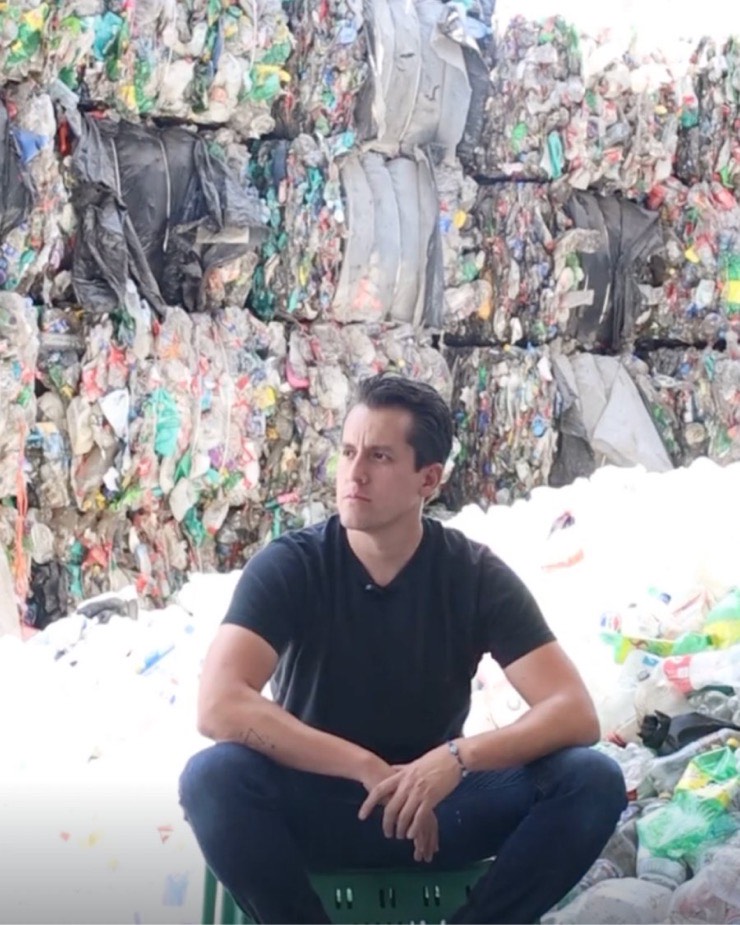 Edgar Temores sentado sobre una caja frente a una pared de pacas de botellas de plástico comprimidas