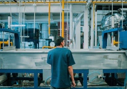 Operario de espaldas frente a una línea de producción con tuberías y tanques