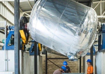 Tanque cilíndrico de acero inoxidable montado sobre su estructura, con operarios de casco azul trabajando debajo