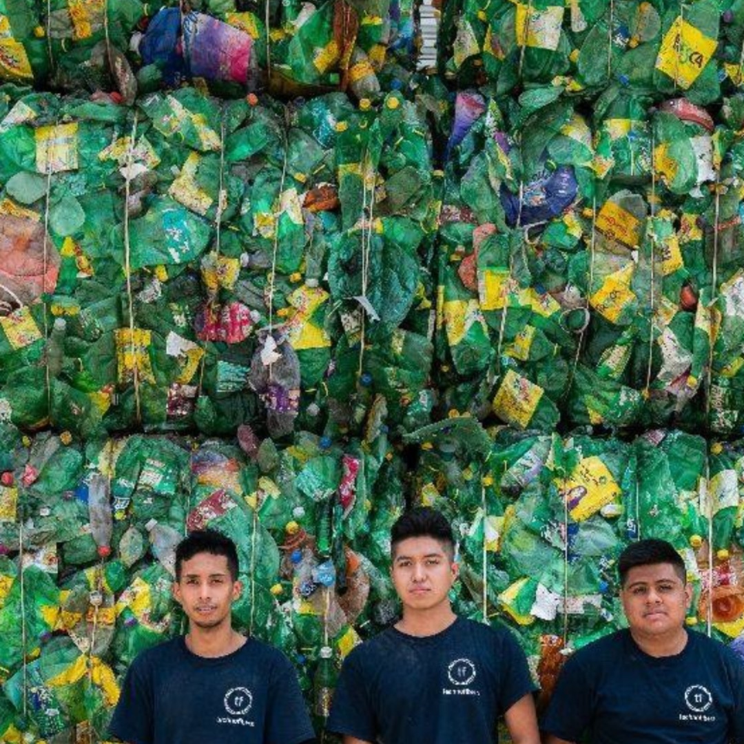 Tres integrantes del equipo de Technofibers frente a una pared de pacas de botellas de plástico verdes
