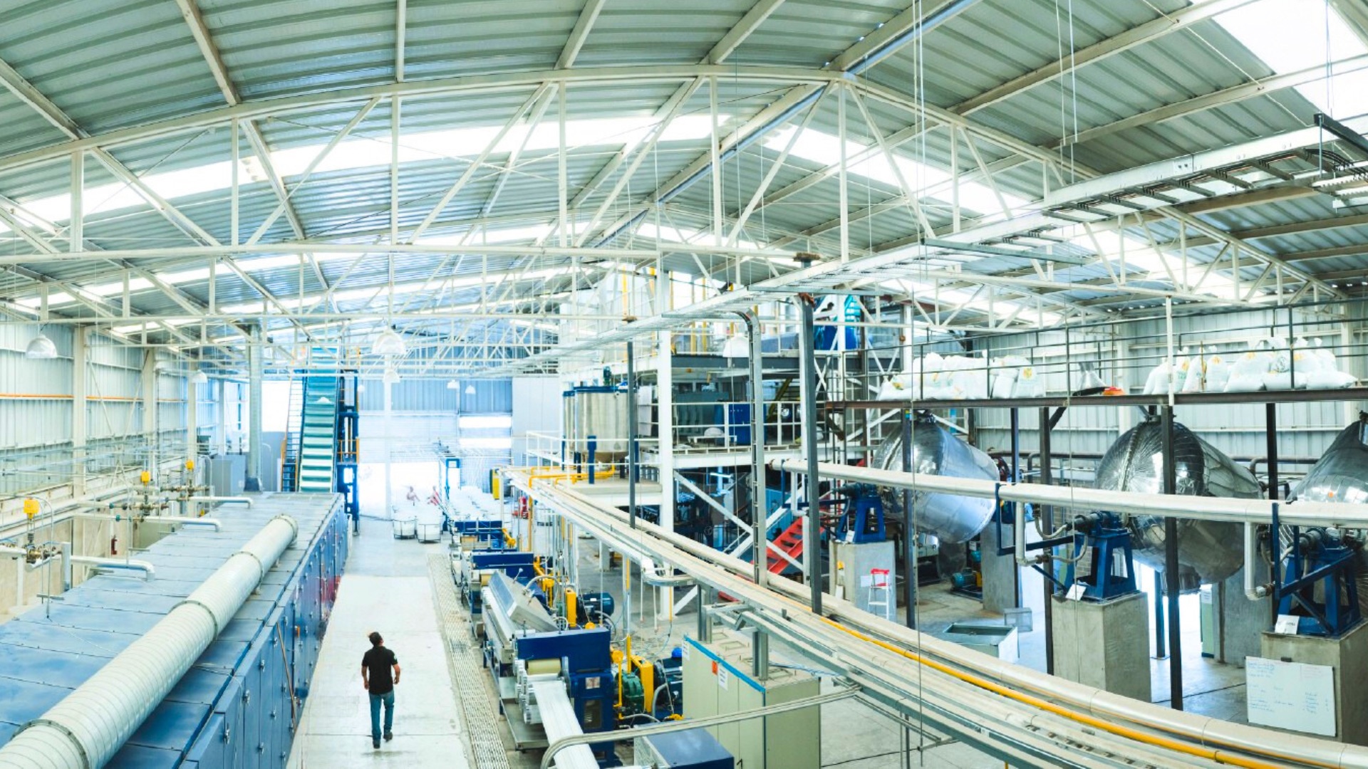 Vista elevada de la nave de Technofibers: las líneas de producción a ambos lados del pasillo central y una persona caminando por él